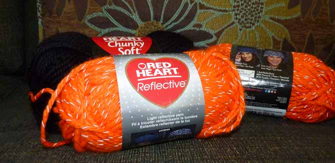 Two balls of orange reflective yarn with a ball of black yarn in the background