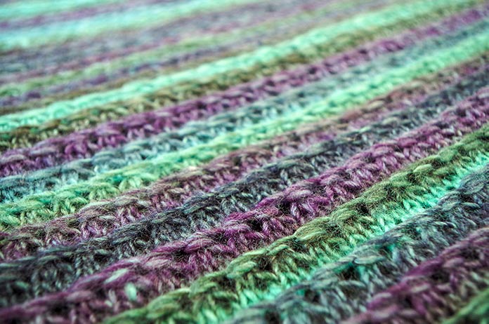 Close up of the triangular shawl textured stitch, ‘Linked chain ridges’ in charcoal, purple and turquoise. This is the Aurora Borealis colorway of Colorburst.