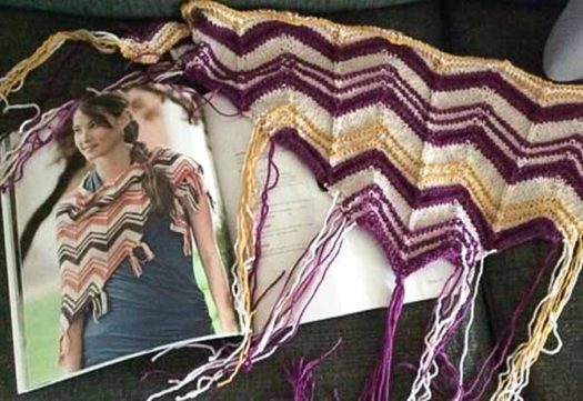 A photo of a ripple shawl with oatmeal, orange, and brown with a sample made in oatmeal, purple, and thin gold stripes beside it