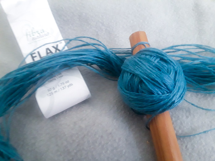 A skein of Fibra Natura FLAX Yarn in the color Adriatic, partially wound on a nostepinne