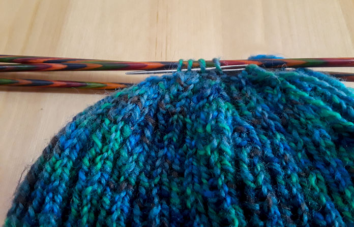 A UNIQUE Knitting Round Tip Yarn Needle inserted into live knit stitches. The stitches are on Knit Picks Wooden Double-Pointed needles.