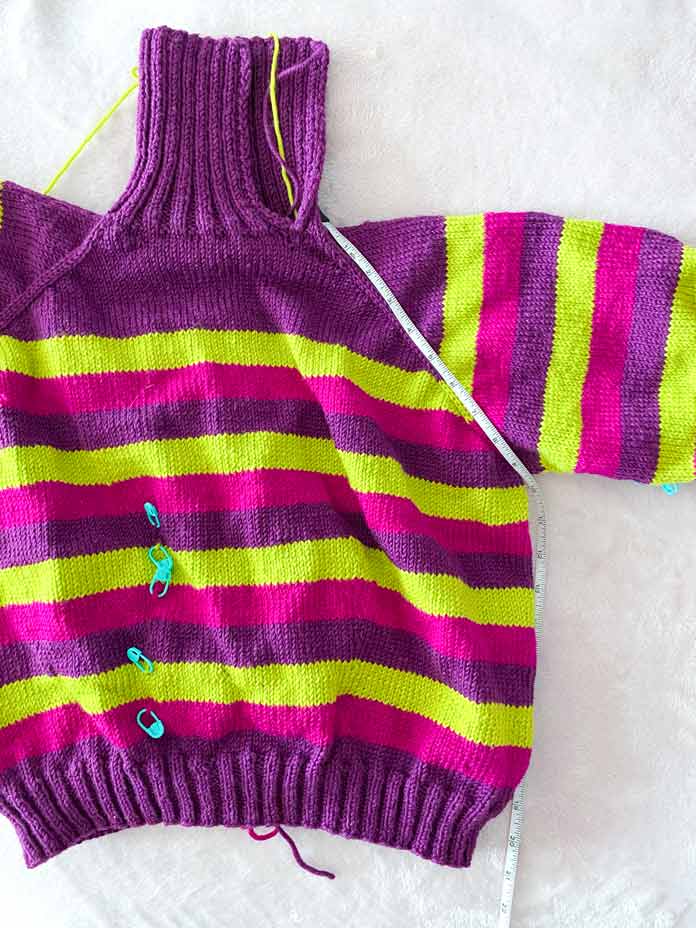 A striped knitted pullover with stitch markers and a measuring tape.