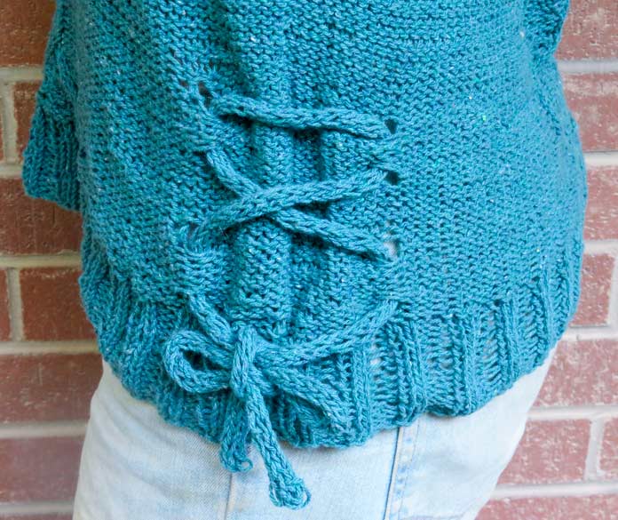 The bottom half of the Palomar Top, knit in Bella Tweed Yarn in Care colorway An I-cord has been threaded through eyelets at the side hem and tied in a bow