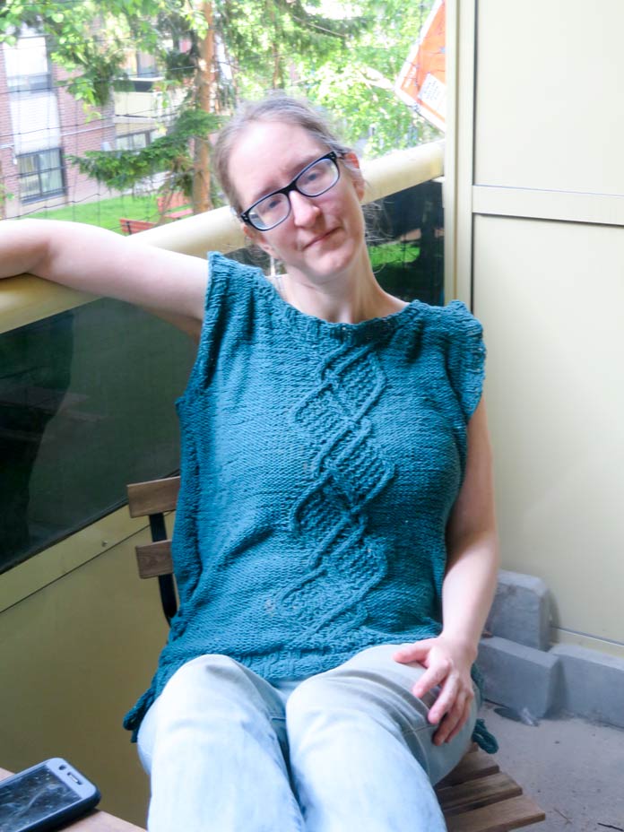 Alt Text Sarah Dawn wearing the completed Palomar Top, knit in Bella Tweed Yarn in Care, featuring a front cable motif and side I-cord ties.