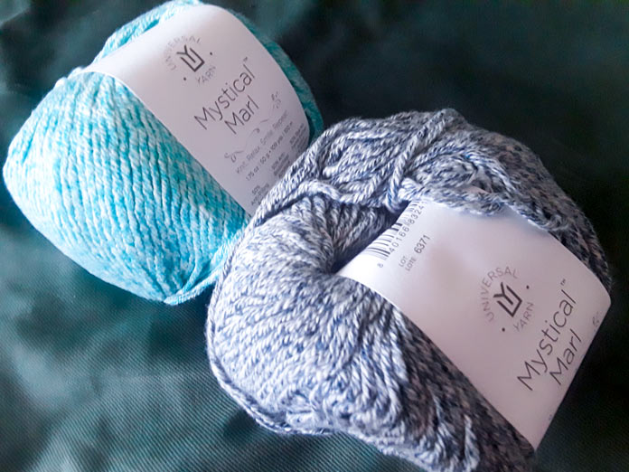 Two balls of UNIVERSAL YARN Mystical Marl in “Lagoon”, which is a bright blue-teal, and “Midnight”, which is a dark blue-gray
