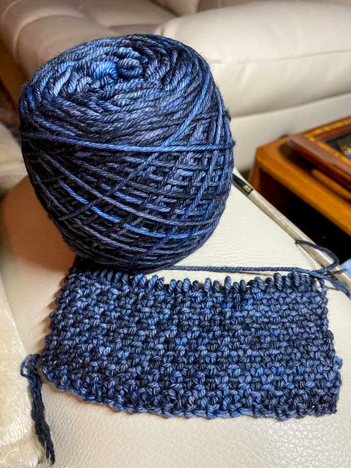 A ball of blue yarn with a knitted swatch in linen stitch