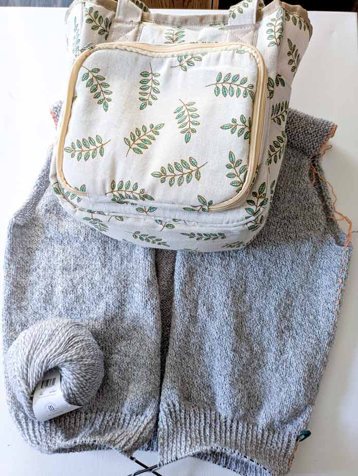 The knitted body of a top-down cardigan beside a project bag.