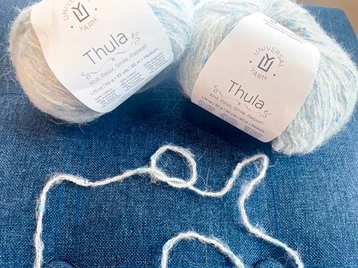 2 balls of yarn and a strand of yarn tied in a loose knot on a blue surface. 