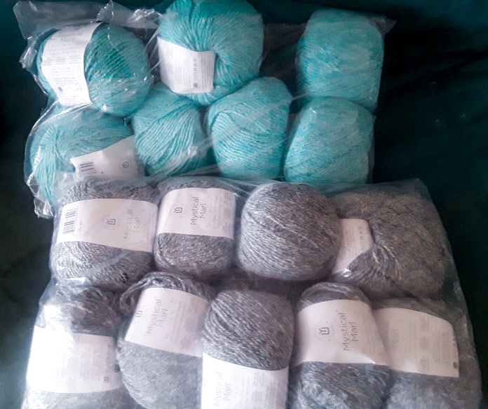 Two clear bags of UNIVERSAL YARN Mystical Marl. One bag in “Lagoon”, which is a bright blue-teal, and the other bag in “Midnight”, which is a dark blue-grey