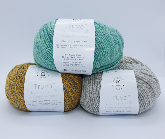Three balls of yarn in heathery tones are stacked in a pyramid. On top is Aegean, predominantly seafoam green with light blue and white twisted in. On the bottom (left) is Medallion, mostly gold with a medium gray and off-white, and Sandcastle (right), a twisty blend of beige with off-white and white added for texture; Truva by Universal Yarn