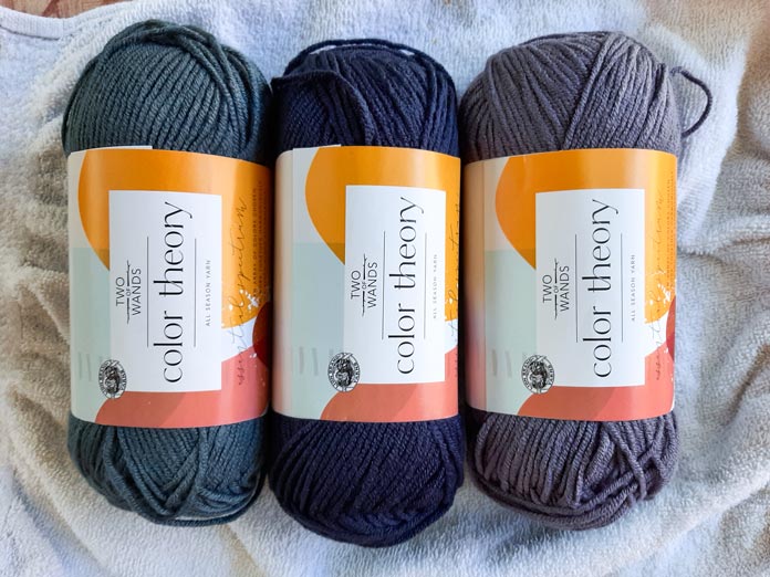 Skeins of Lion Brand Color Theory in colors Amethyst, Admiral and Stonewash side by side on a white background