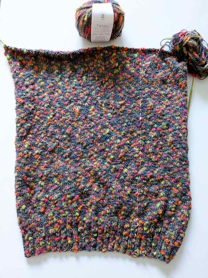 The finished back of the Lawson Cardigan, live stitches still on the needle and a ball of yarn.