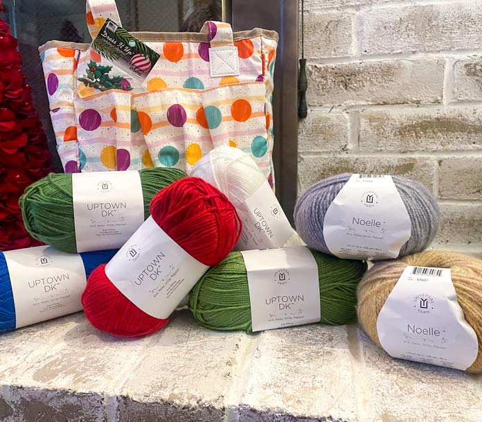 7 balls of yarn, a knitting tote, a package of embellishments on a brick fireplace and a Christmas ornament 