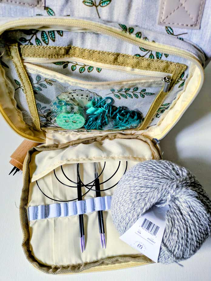 The knitting supplies are organized in a beautiful project bag with pockets for needles and notions