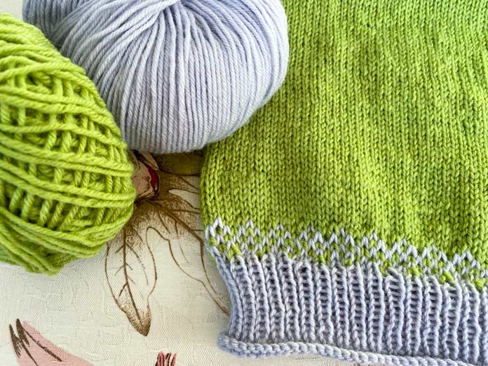 2 balls of Universal Yarn Deluxe DK in Lime Tree and Ice Rustic colorways and the color stranded knitted bottom edge of the Jay Sweater; using LANTERN MOON Destiny Ebony knitting needles.