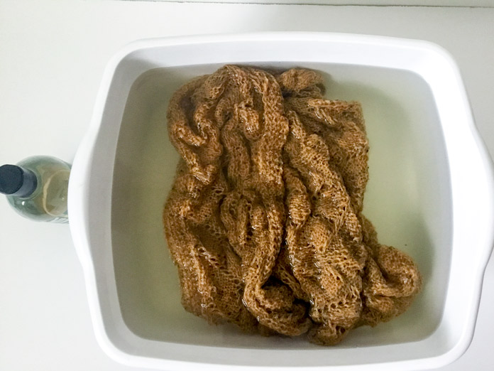 The finished ochre Arum Shawl in a bowl of warm water next to a bottle of Soak detergent