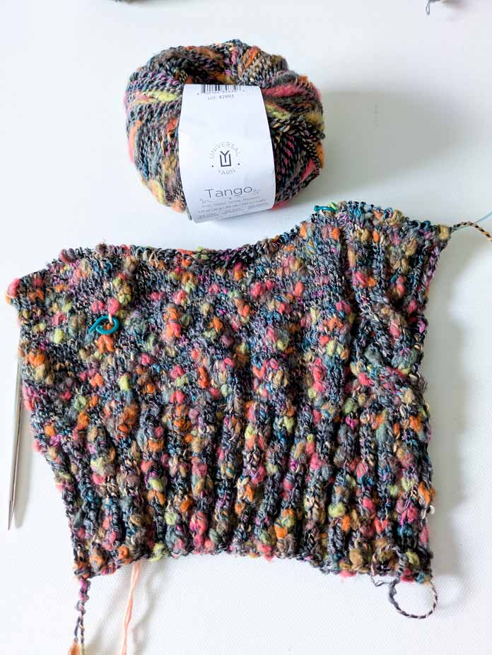 A ball of yarn with label and the knitted right front of the cardigan with the cable motif; UNIVERSAL YARN Tango