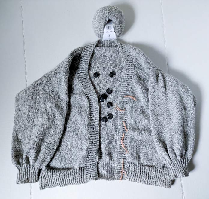 The front view of the finished cardigan, the buttons to be sewn and a ball of yarn.