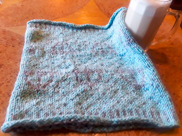 The Holland Cowl lying flat. It's a colorwork cowl knit in two colors of UNIVERSAL YARN Mystical Marl, and it has a centered tulip motif.