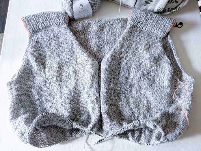 The body of a grey knitted cardigan on the needles.