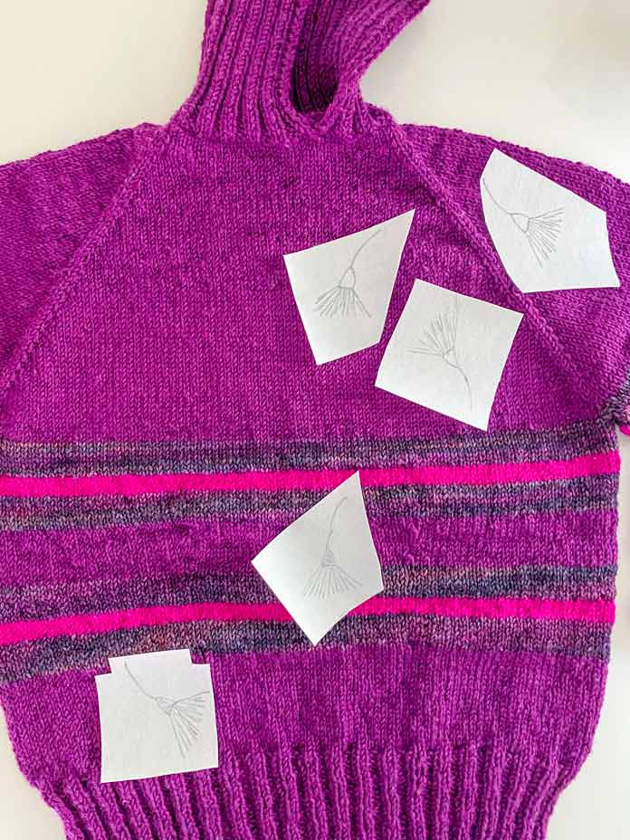 Pieces of Sulky Sticky Fabri-Solvy with flowers drawn on them on a knitted pullover; embroidery on knits