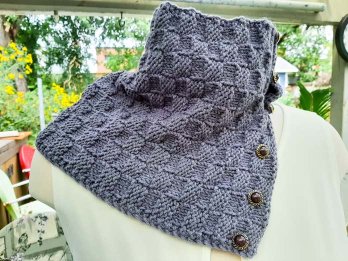 A completed cowl in the Lion Brand Color Theory Amethyst is on the neck of a figure form with the lower buttons open.