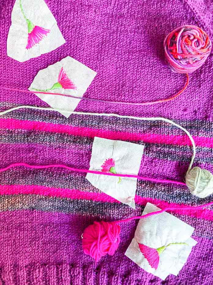 Three balls of leftover yarn laid out on a knitted pullover; Sulky Sticky Fabri-Solvy, DMC floss, DMC Chenille needles