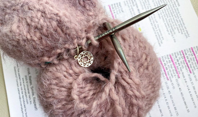 Yarn with knitting needles resting on knitting instructions.