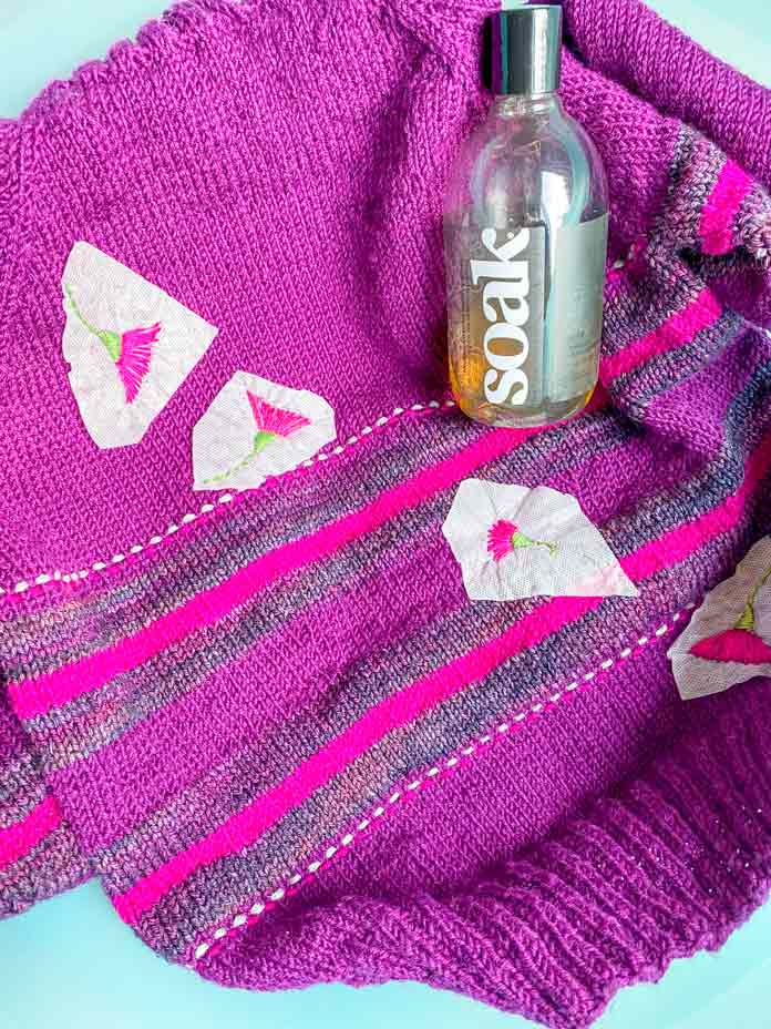 A bottle of Soak Wash on a knitted pullover in a washtub; Sulky Sticky Fabri-Solvy, DMC floss, DMC Chenille needles