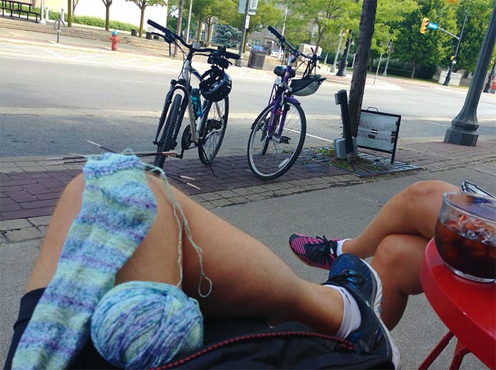 Two cyclists are having a coffee in a road-side patio in Welland Ontario. The male is knitting a sock with Bamboo Pop Sock.