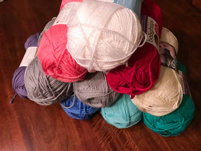 A pyramid of Red Heart's Baby Hugs Medium and Light yarn in 9 of the 18 available colors.