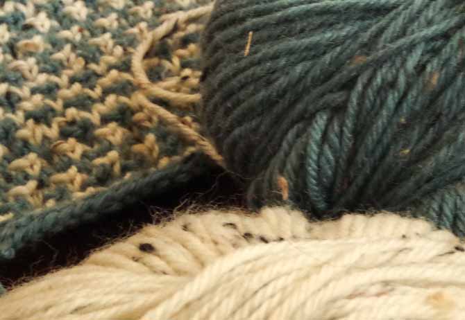 Ball of pine green tweed yarn with black, taupe and camel flecks.