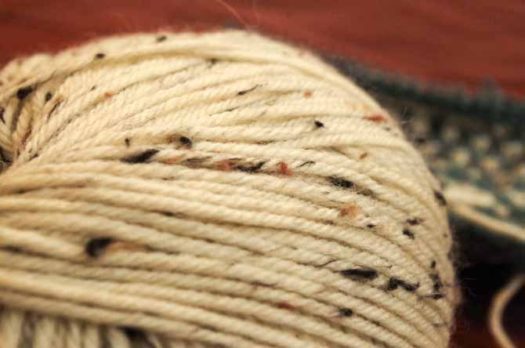 Skein of the off-white Porcelain colorway of Deluxe Worsted Tweed Superwash which has black, camel and taupe flecks.