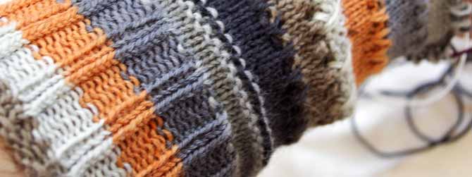 close up of cuff-down sock worked in a Prose yarn with stripes in off white, grey, medium brown-grey, charcoal and orange.