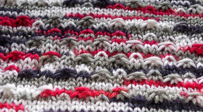 A top-down view of the fleck stitch in Red Heart Super Saver Pooling shows off the texture of this red, gray, white, and black yarn the best.