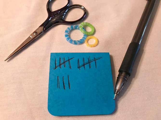 Post it notes and a pen are used to keep tally marks. A pair of scissors and stitch markers are also in the frame.