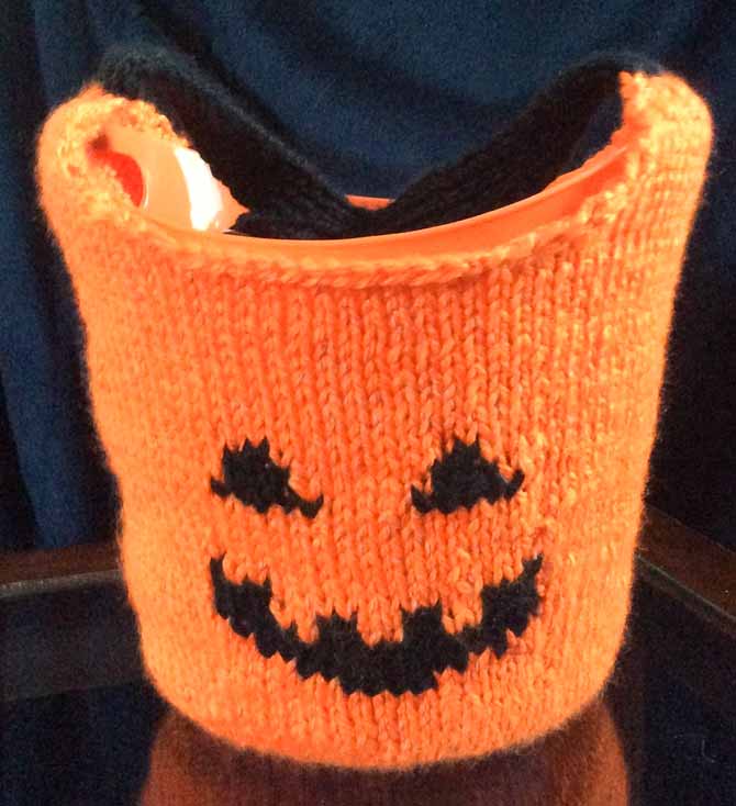 An orange jack-o-lantern bag with a plastic lining sitting on a table with a dark backdrop.