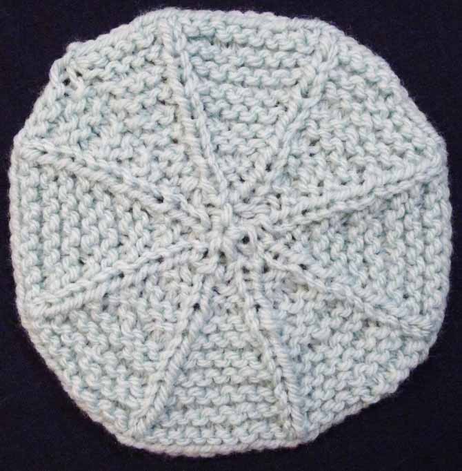 A knitted garter stitch circle made of mint yarn with knit-stitch "spokes" that radiate out from the center of the work